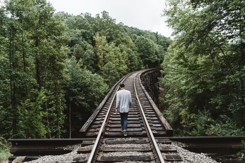 man-standing-on-railway-surrounded-by-trees